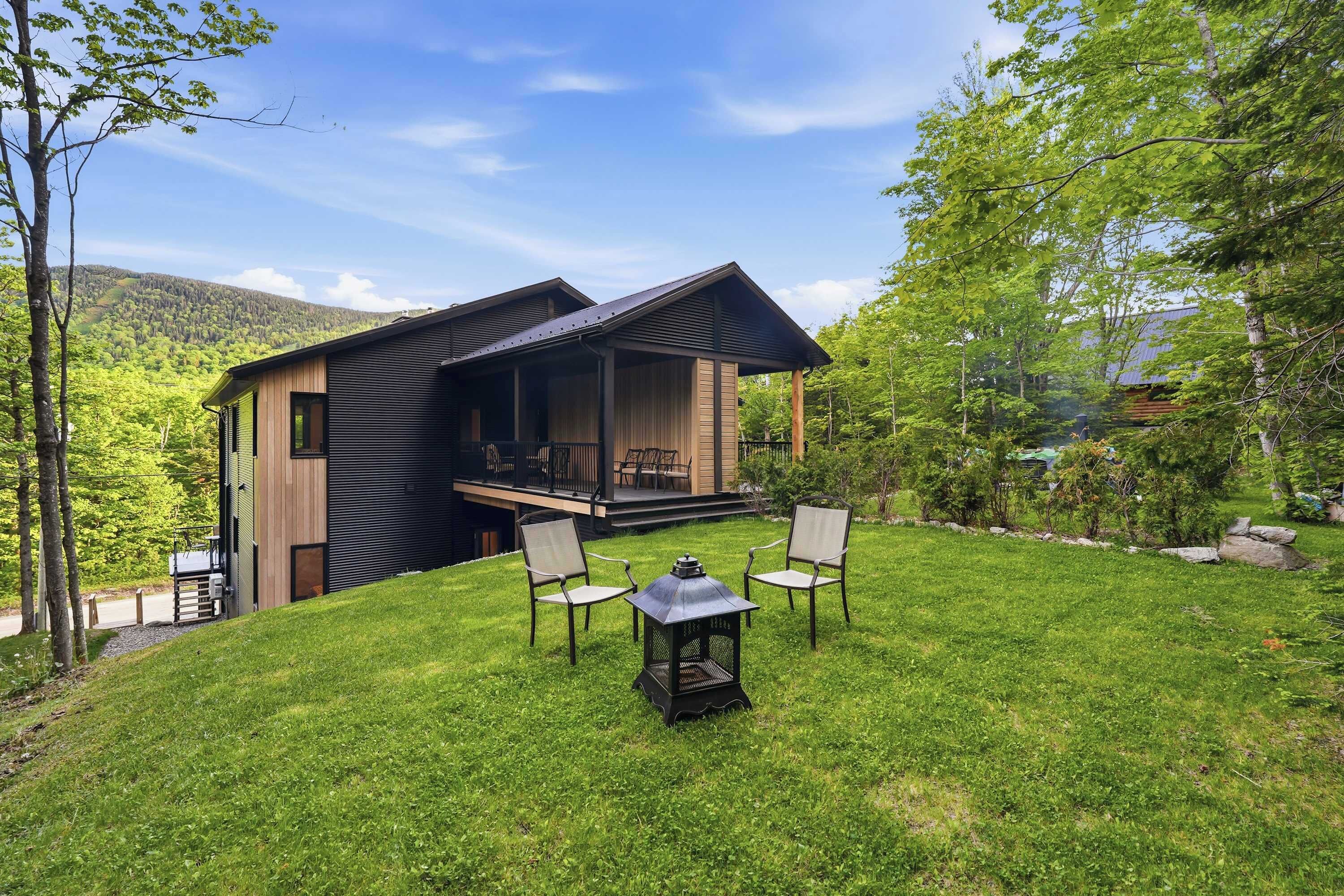 Uma casa moderna com varanda coberta, gramado e área de estar com cadeiras e mesa.