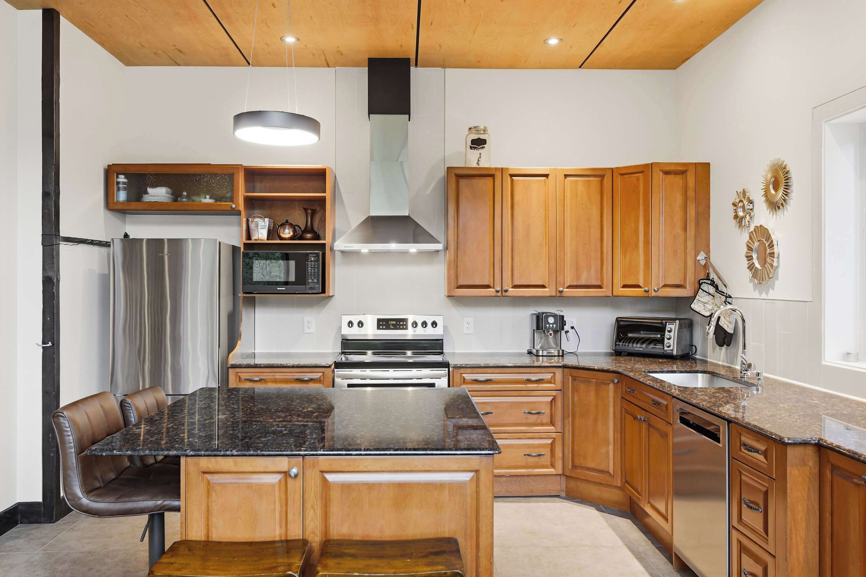 Una cocina moderna con una isla central, electrodomésticos de acero inoxidable, armarios de madera y una lámpara colgante.