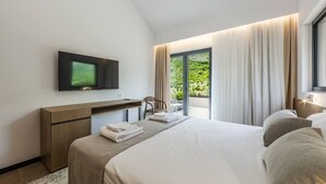 A modern hotel room with a large bed, a desk, a flat-screen TV, and a balcony with curtains.