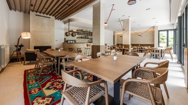 A spacious dining area with wooden tables and chairs, a patterned rug, and pendant lighting.