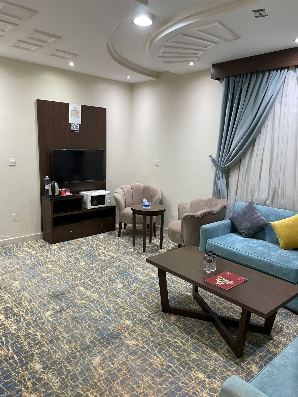 Habitación de hotel con televisión de pantalla plana, un sofá, una mesa de centro y una alfombra estampada.