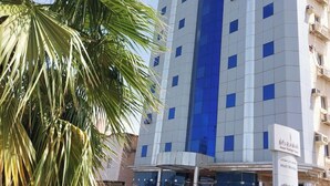 A multi-story hotel with a prominent blue facade, a central entrance, and a palm tree in the foreground.