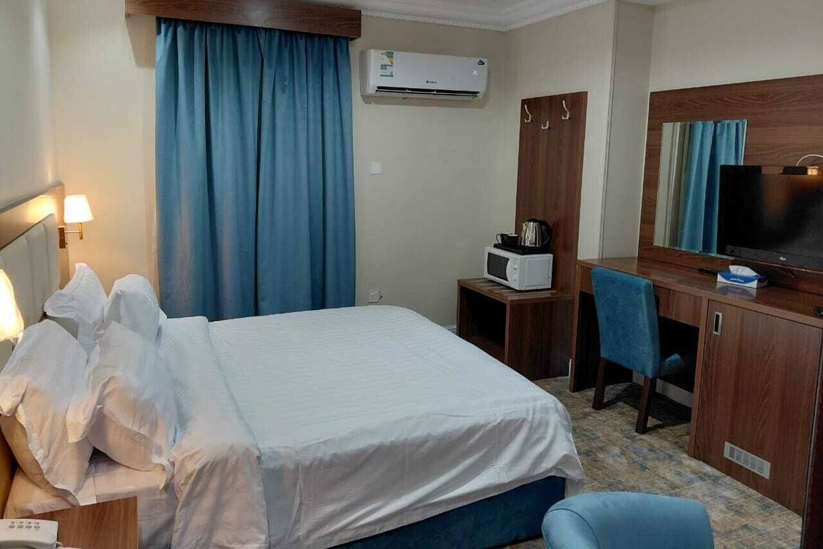 Ein Hotelzimmer mit einem Bett, einem Schreibtisch mit Computer, einem Fernseher und einer Klimaanlage.