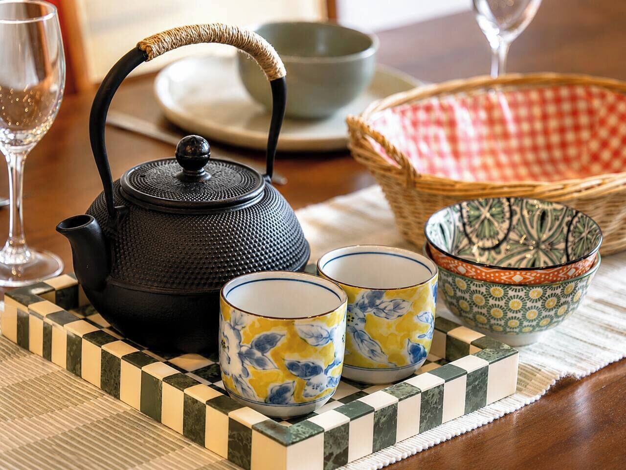 A tea set with a black kettle, two cups with floral patterns, and a decorative bowl on a checkered tray.