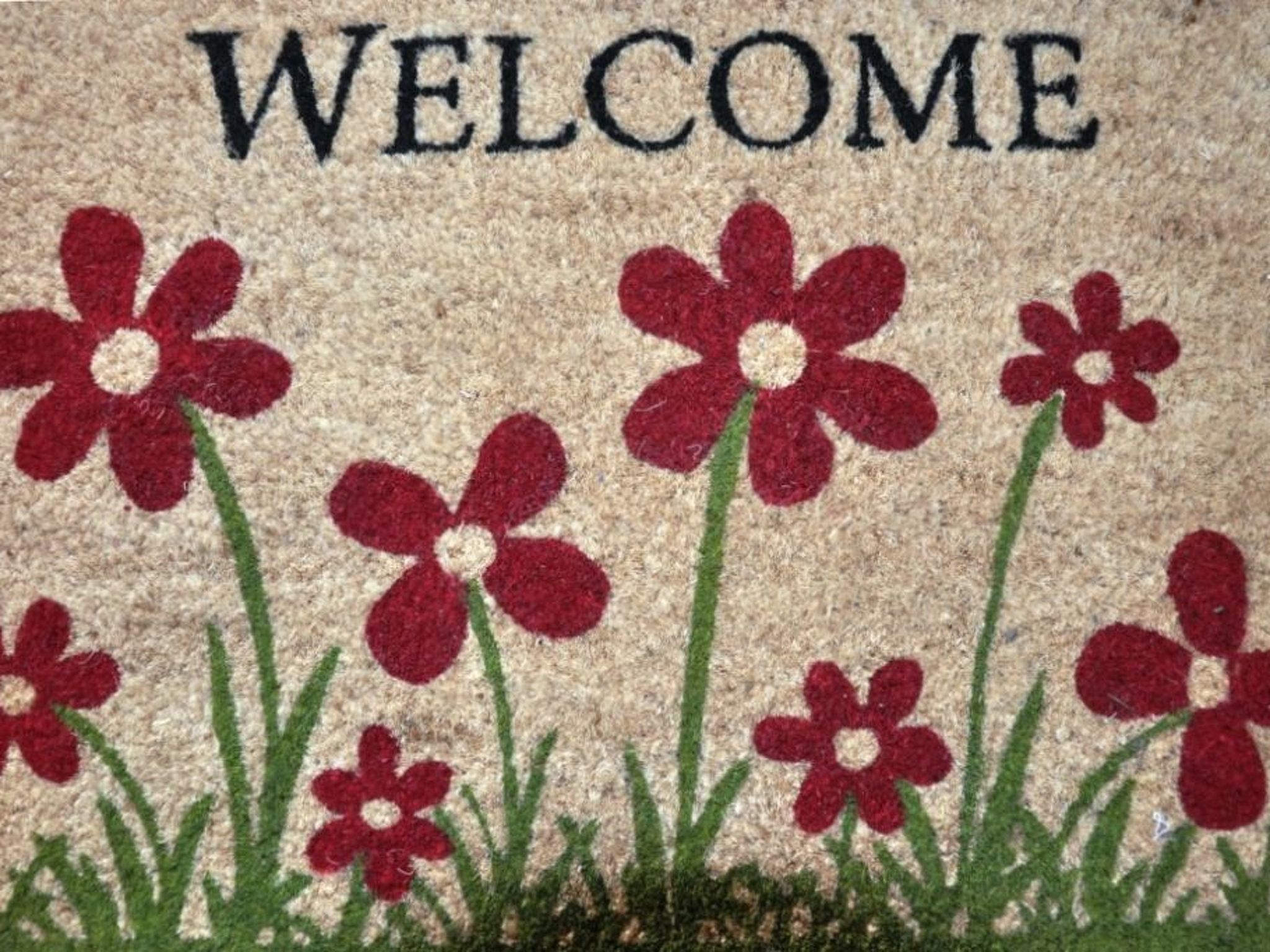 A welcome mat with red flowers and green grass.