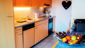 Una cocina con armarios de madera, lavavajillas, cafetera y frutero sobre la encimera.