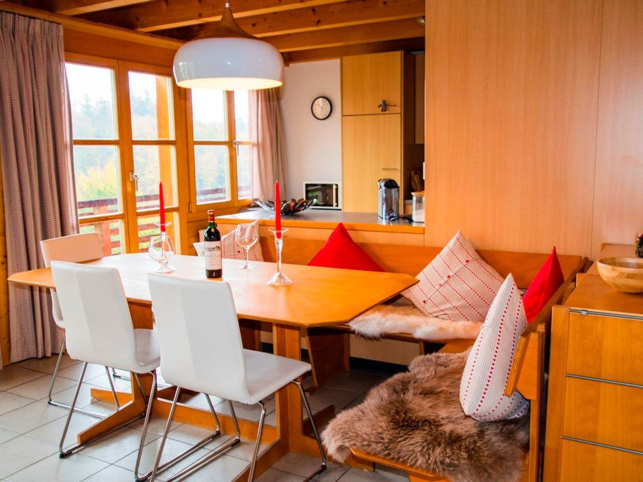A cozy dining area with a wooden table, white chairs, and a bench with red cushions.