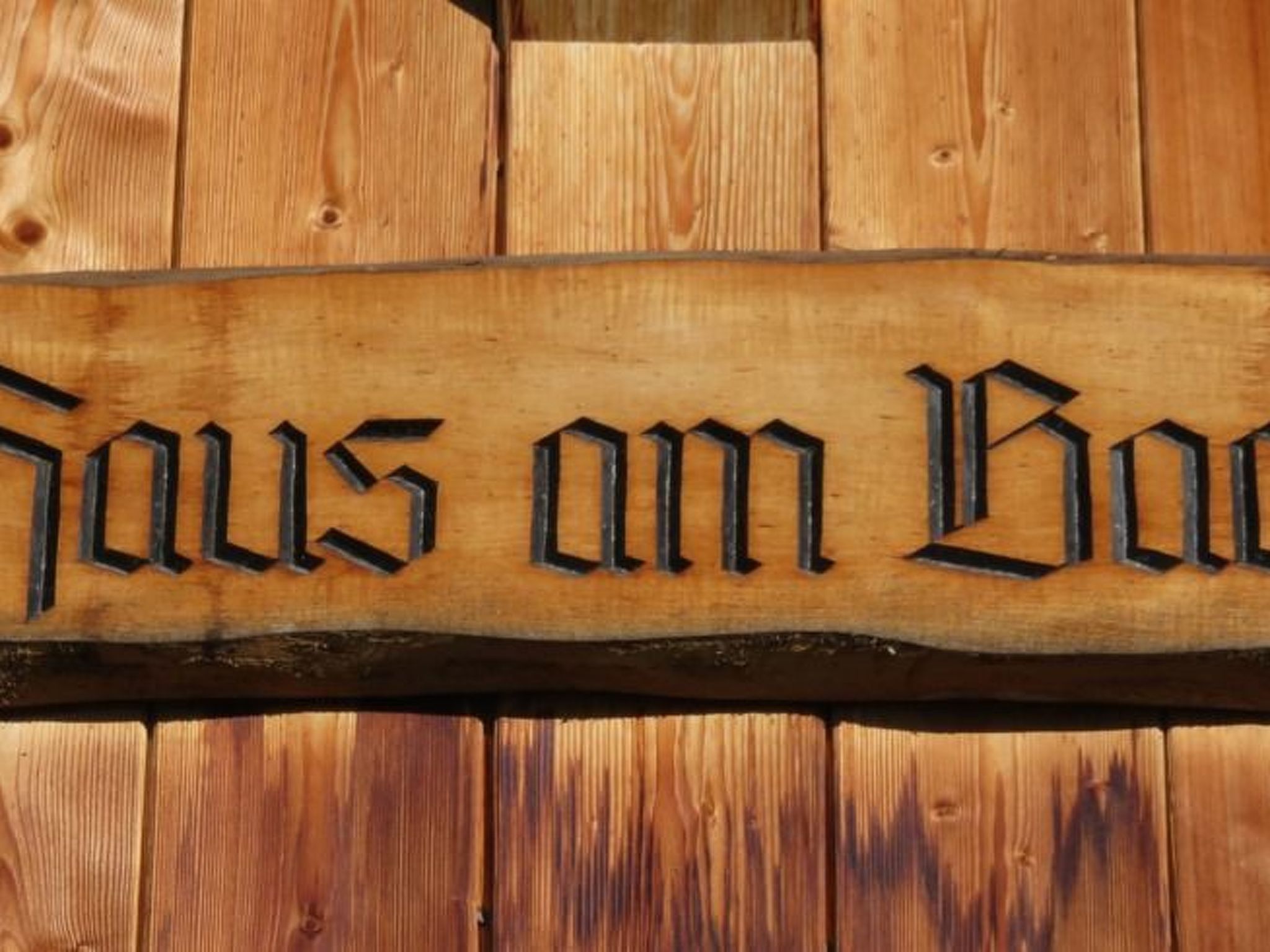 A wooden sign with carved text, mounted on a wooden background.