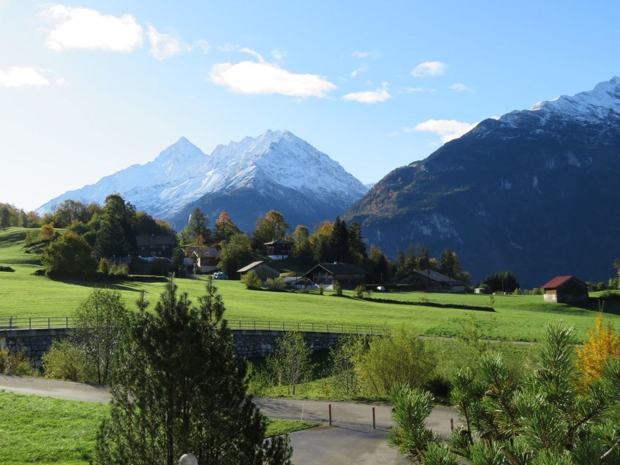 Paisaje rural con una cadena montañosa, casas y un campo verde.