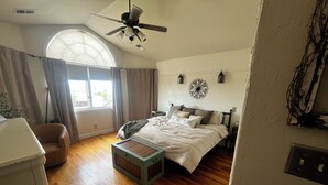 A bedroom with a bed, a ceiling fan, a window with curtains, a bedside table, and a lamp. - Spacious 5-bedroom house in Cheyenne with AC, fitness room, outdoor space (Cheyenne)