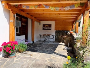 Eine Holzhütte mit einer Steinterrasse, einem Tisch mit Stühlen und einem Schild mit der Aufschrift 'STUBELI'.