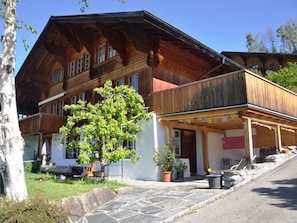 Ein traditionelles Holzhaus mit geneigtem Dach, einer Veranda und einem Steinweg, der zum Eingang führt.