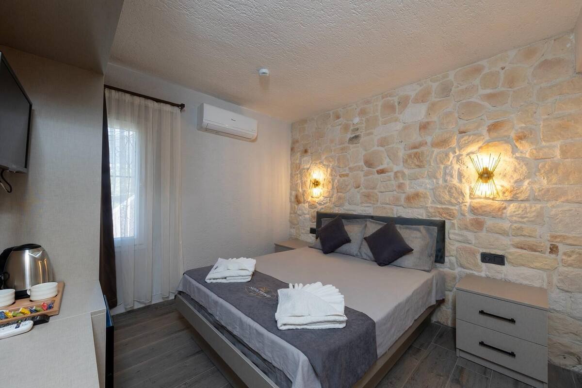 Habitación de hotel con pared de piedra, cama con dos almohadas, mesita de noche, televisor y cafetera.
