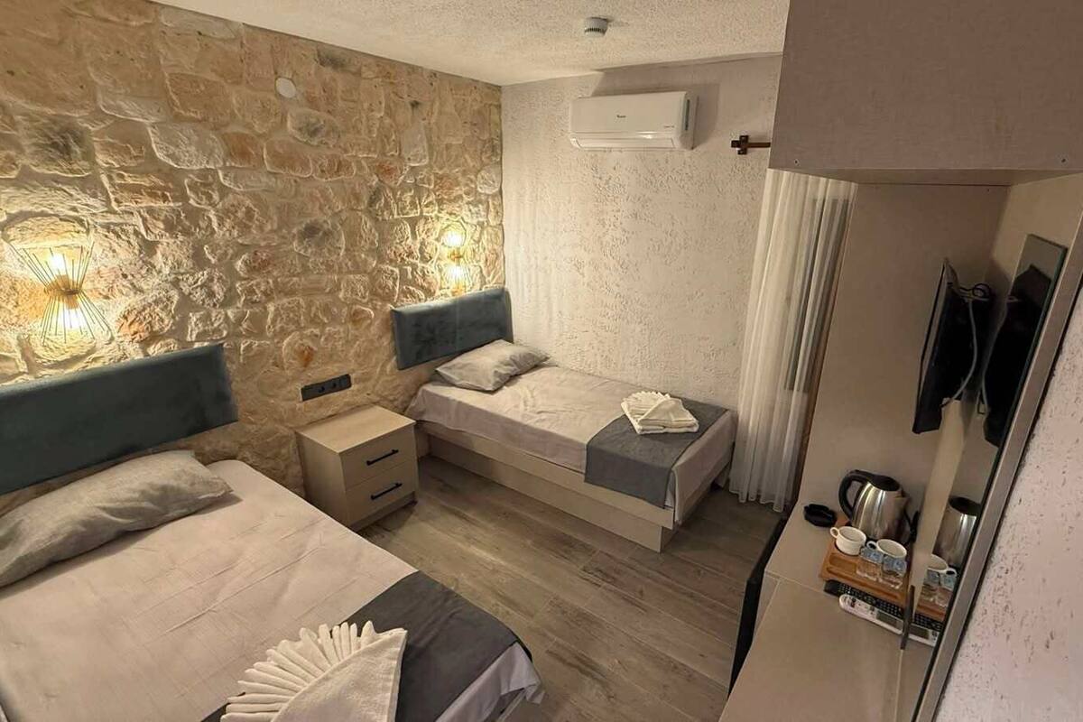 Un dormitorio con pared de piedra, dos camas, una mesita de noche y un espejo, con una ventana con cortinas.