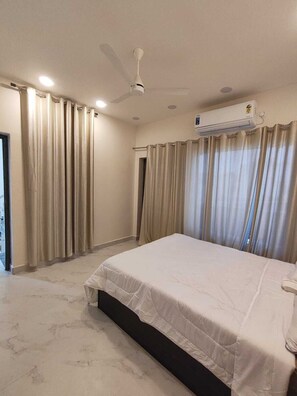 A bedroom with a bed, curtains, a ceiling fan, and an air conditioning unit. - AGV Stay (Tiruvannamalai)