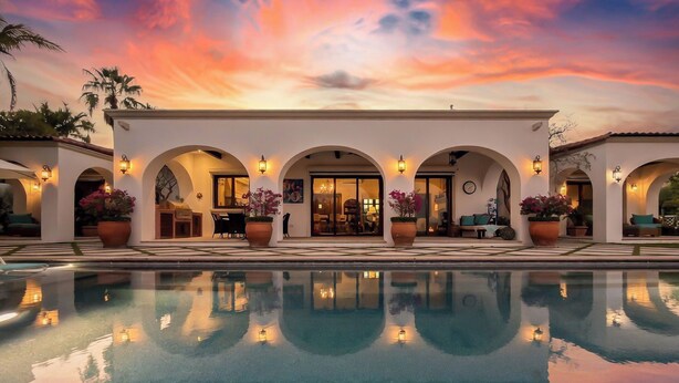 Zona junto a la piscina con vista al atardecer, paseos en arco y plantas en macetas.