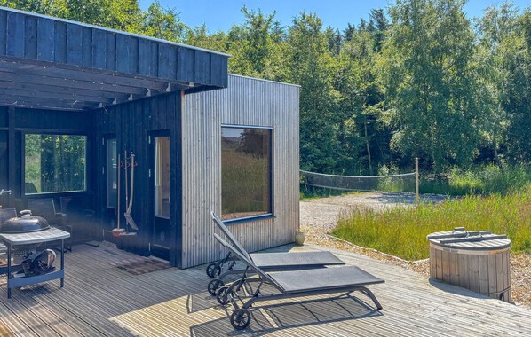A modern wooden cabin with a deck, outdoor seating, and a sauna.
