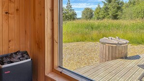 Eine Holzhütte mit Kamin aus Stein, einer Holzdiele und Blick auf ein Wiesenfeld.