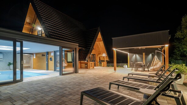 Een modern buitenzwembad met ligbedden, een overdekte zithoek en een gebouw met een schuin dak.