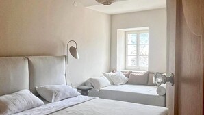 Ein Zimmer mit zwei Betten, einem Nachttisch, einer Lampe, einem Fenster und einer Tür.