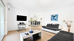 Una sala de estar moderna con un televisor de pantalla plana, un sofá, una mesa de centro y un comedor al fondo.