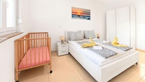 Un dormitorio con una cuna, una cama con almohadas estampadas, una mesita de noche y un cuadro colgado en la pared.