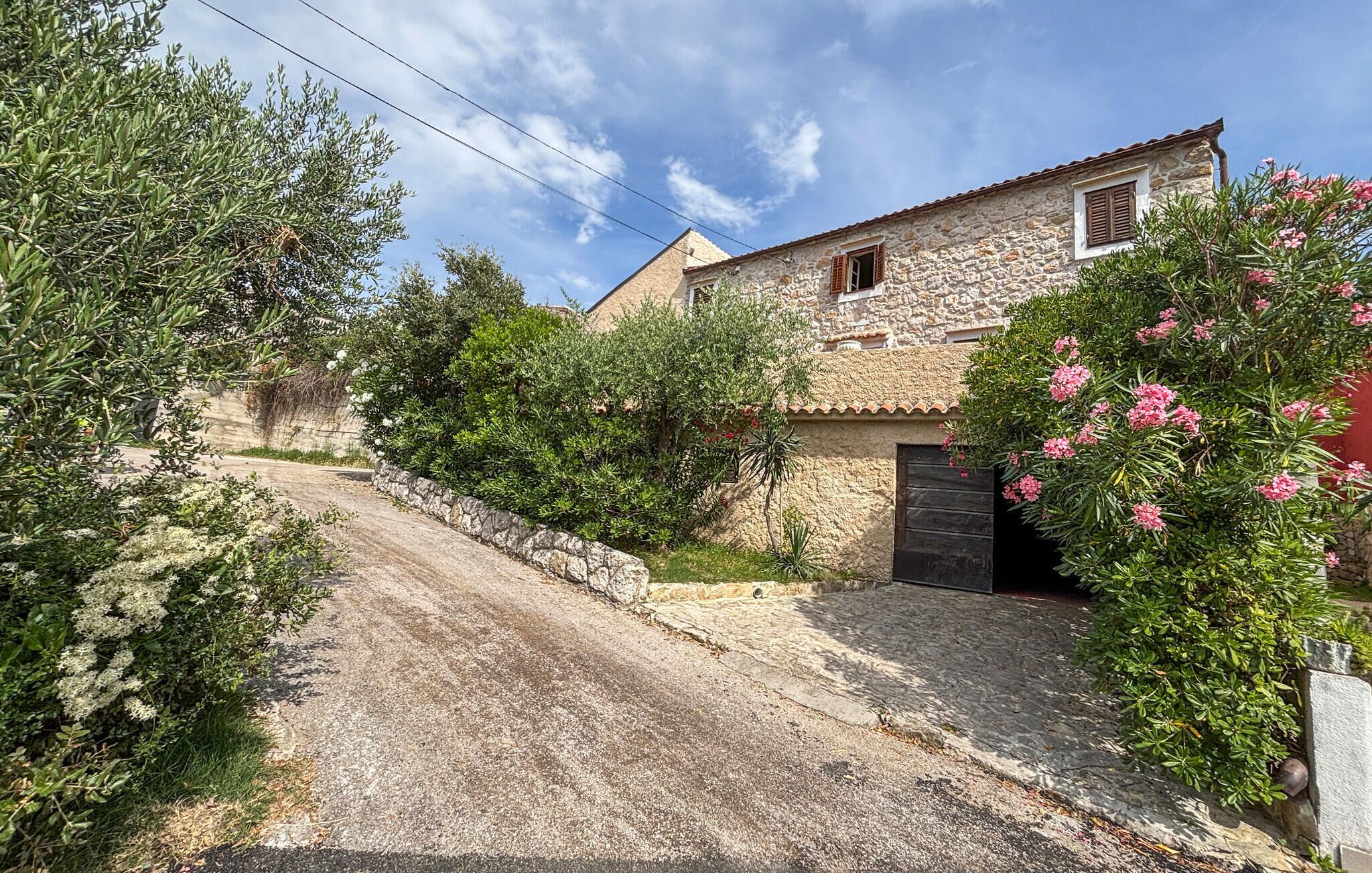 Une maison en pierre avec une allée pavée, entourée d’une végétation luxuriante et de plantes en fleurs.