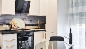 A modern kitchen with white cabinets, a black countertop, a large decorative shell, and a glass table with wine glasses. - 1 bedroom lovely apartment in Rab Barbat (Rab Barbat)