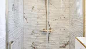 A bathroom with a glass shower enclosure, marble walls, and a gold shower head. - 1 bedroom lovely apartment in Rab Barbat (Rab Barbat)