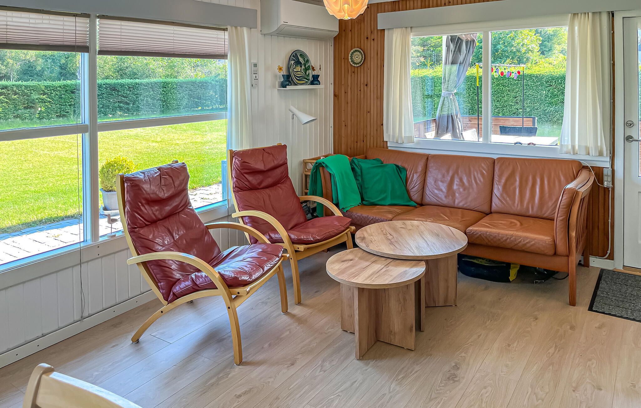 Ein Zimmer mit Holzboden, einem braunen Ledersofa, zwei Ledersesseln, einem kleinen Holztisch und großen Fenstern mit Jalousien.
