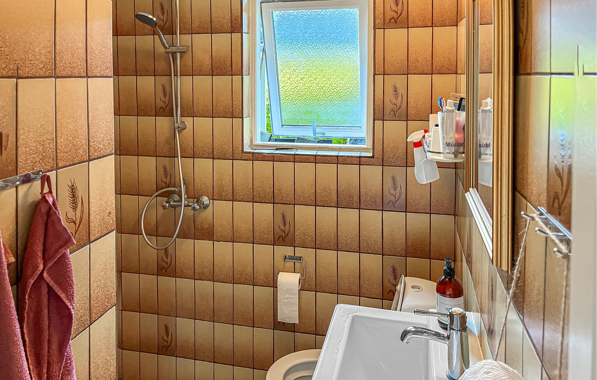 Et badeværelse med bruser, toilet, håndvask og et vindue med udsigt.