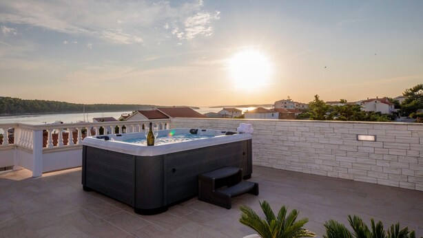 Una vasca idromassaggio su un balcone con vista sul mare e sugli edifici.