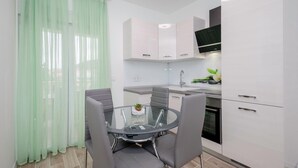 Una cucina moderna con mobili bianchi, un tavolo da pranzo in vetro e una tenda verde.