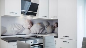 A modern kitchen with white cabinetry, a built-in oven, a stainless steel sink, and decorative shells on the backsplash. - Amazing apartment in Rab Barbat with WiFi (Rab Barbat)