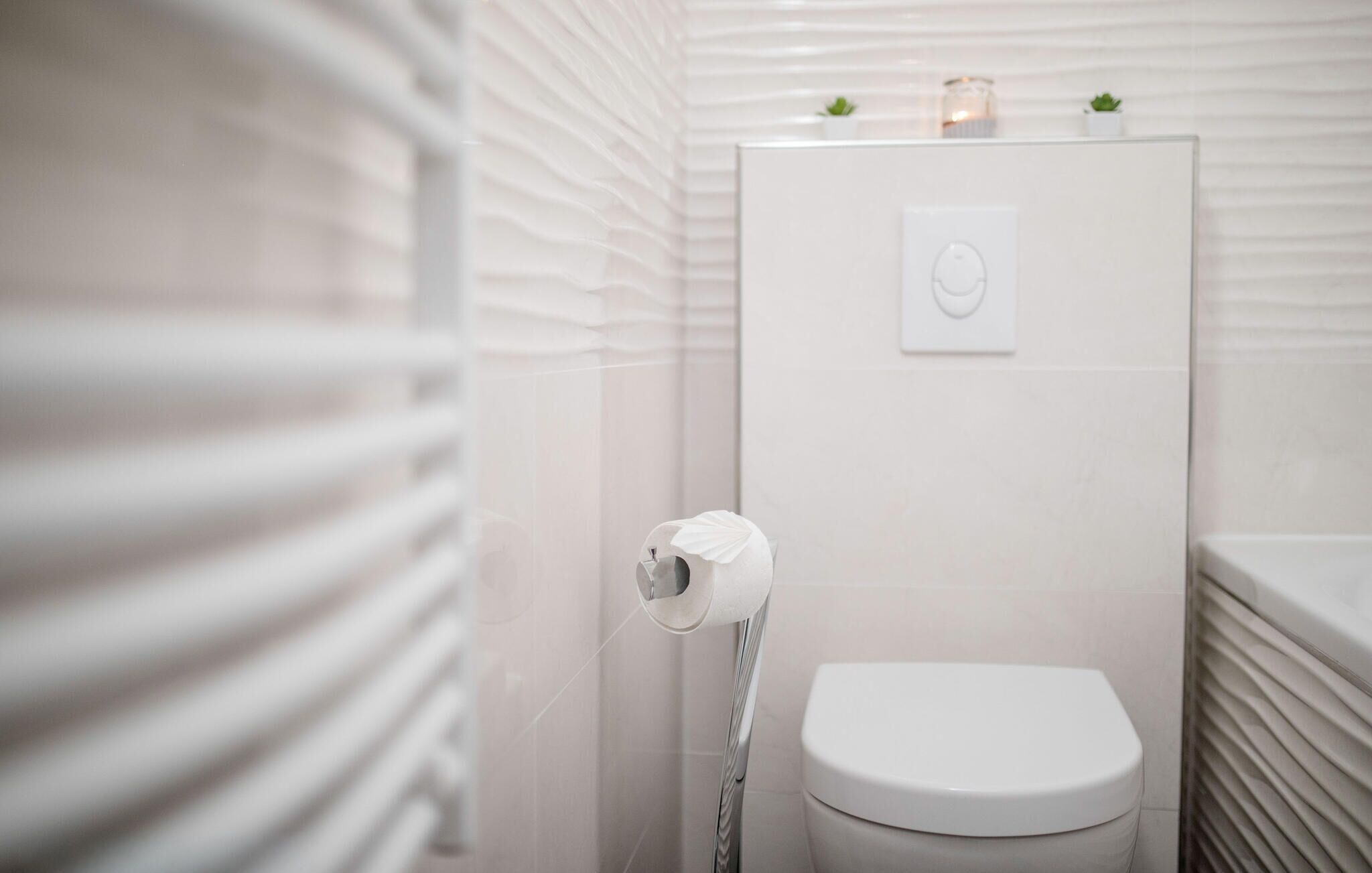 A modern bathroom with a toilet, a towel rack, and a wall-mounted light fixture.