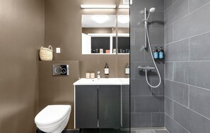 A modern bathroom with a toilet, sink, mirror, and shower. - 1 bedroom beautiful apartment in Ebeltoft (Ebeltoft)