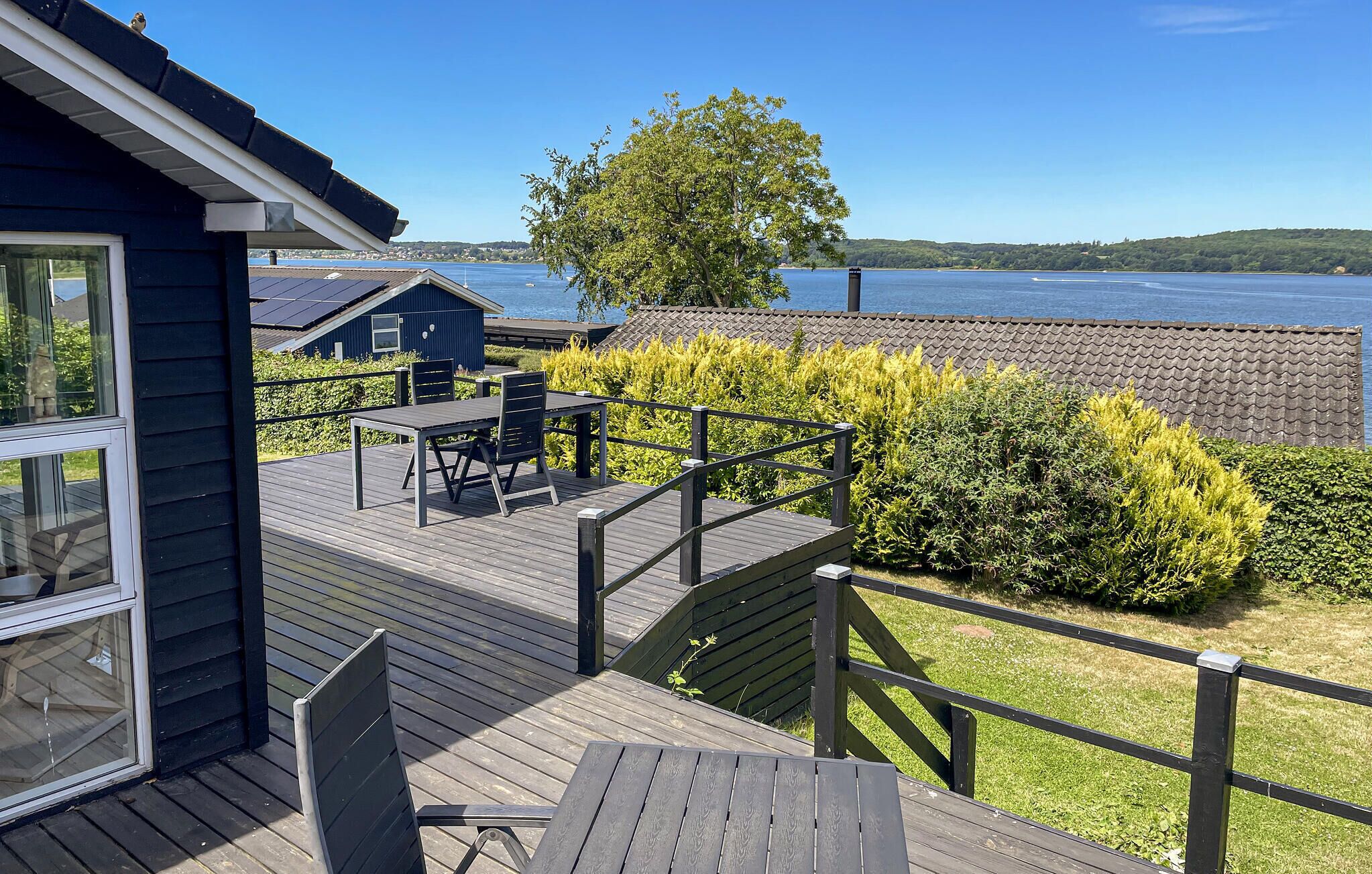Une terrasse en bois avec des meubles d’extérieur, une vue sur un lac et une côte lointaine.