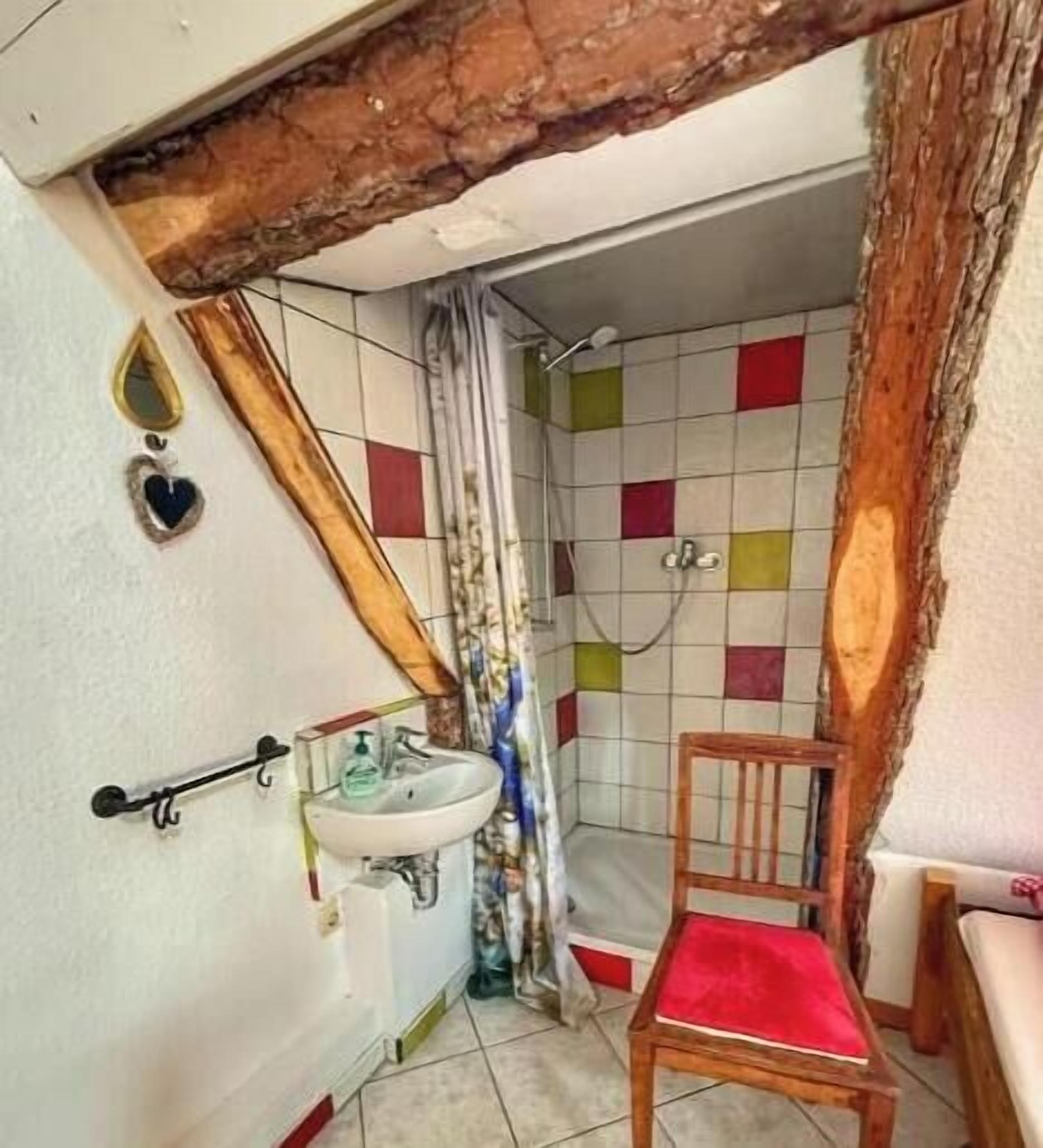 Ein Badezimmer mit Holzstuhl, Waschbecken und Dusche mit farbenfrohen Fliesen.