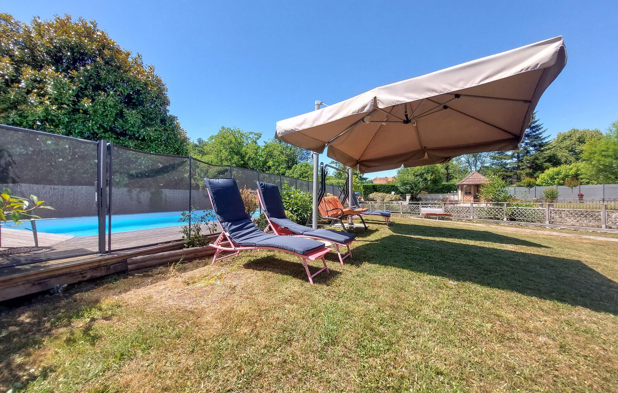 A backyard with a swimming pool, two lounge chairs, and a large umbrella.