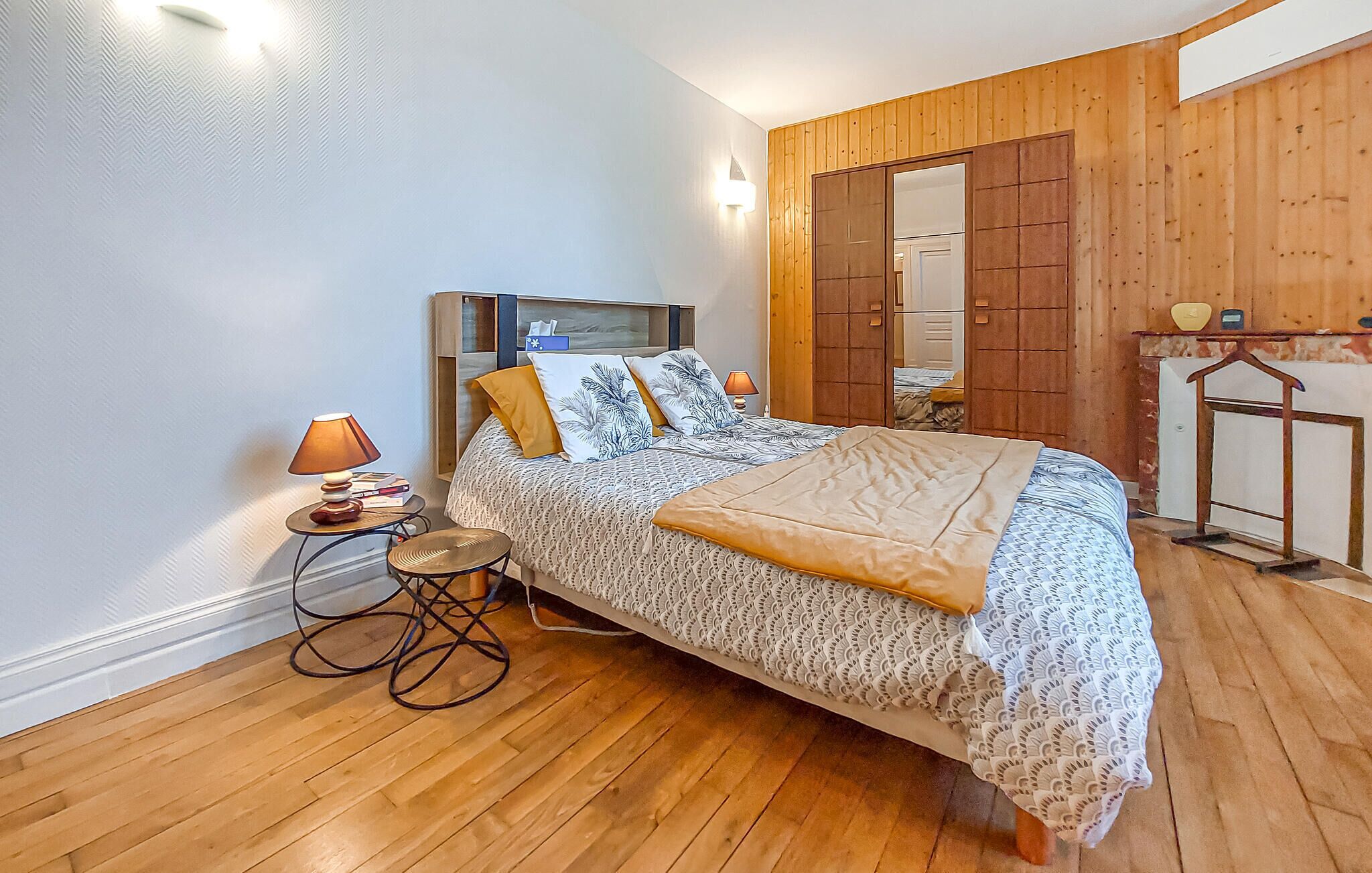 Een slaapkamer met een bed, nachtkastje, lamp en een houten garderobe.