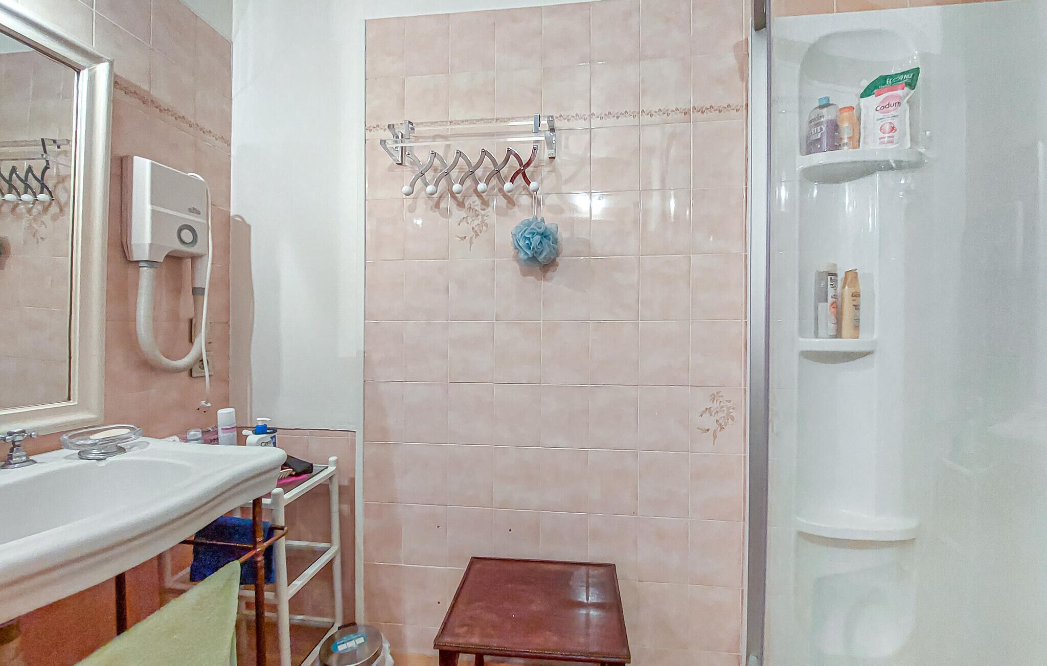A bathroom with a sink, mirror, towel rack, shower, and toiletries shelf.