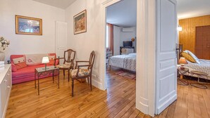 Une pièce avec un plancher en bois, un canapé rose, une table à manger avec des chaises, un lit recouvert d’une couvre-lit à motifs et un téléviseur en arrière-plan.