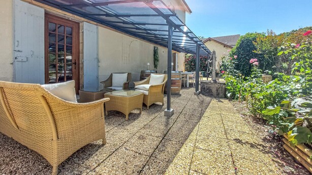 Un espace extérieur abrité, aménagé avec des meubles en osier et une terrasse carrelée en pierre.