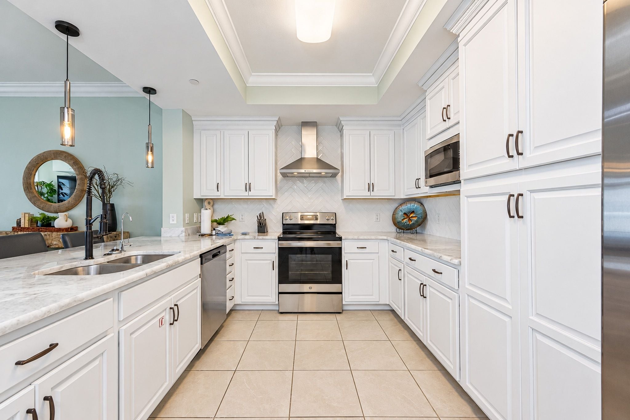 A modern kitchen with white cabinetry, stainless steel appliances, and a herringbone tile backsplash.
