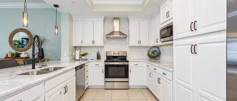 A modern kitchen with white cabinetry, stainless steel appliances, and a herringbone tile backsplash.