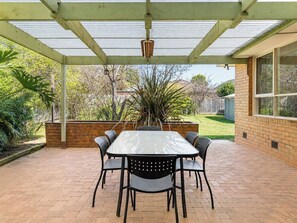 Ein überdachter Patio-Bereich mit Tisch und Stühlen, einer Backsteinmauer und Blick auf den umliegenden Garten.