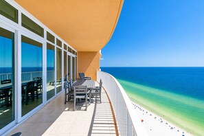 Ein Balkon mit Tisch und Stühlen mit Blick auf einen Strand und klares, blaues Wasser.