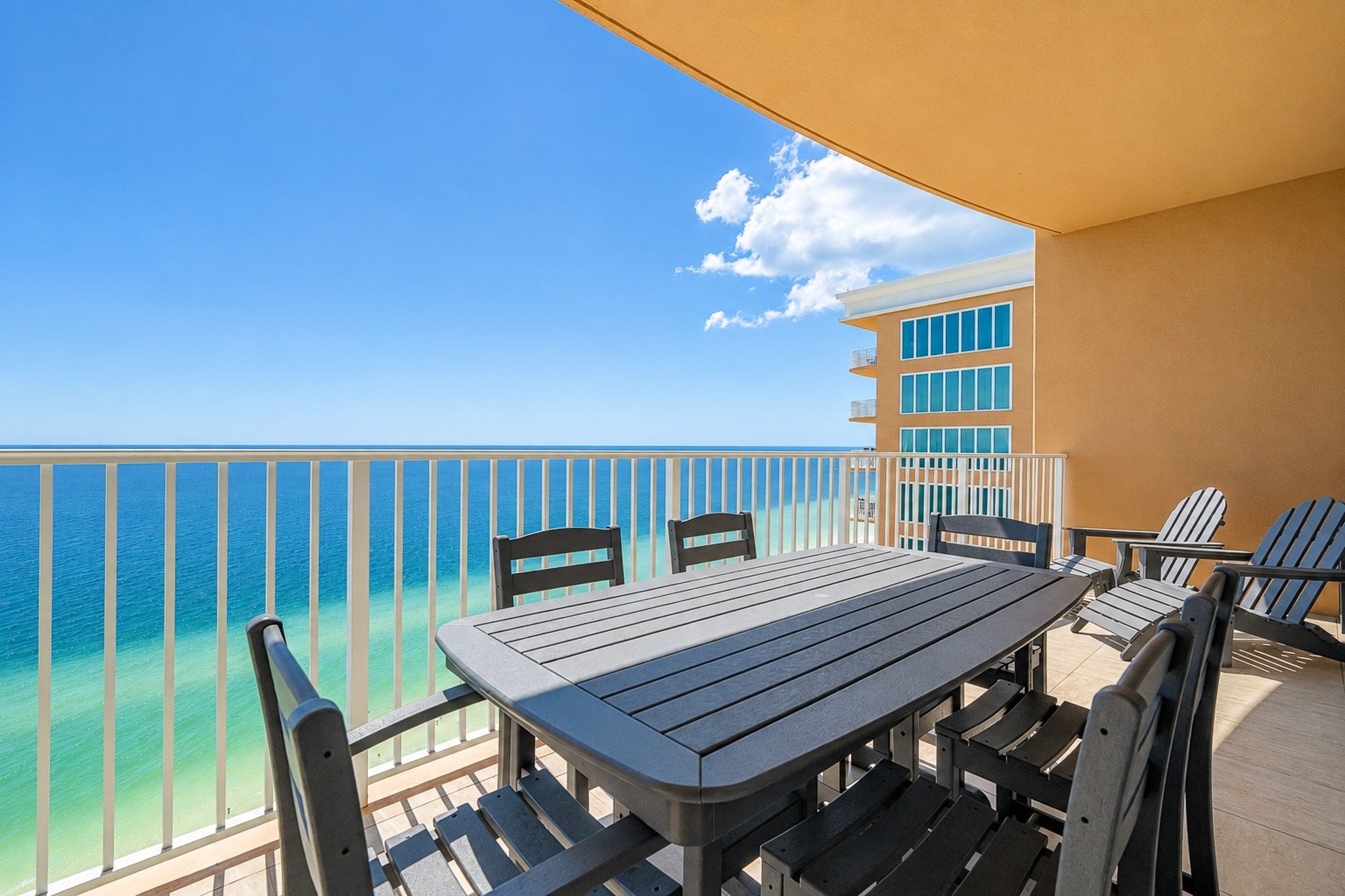 Een balkon met een tafel en stoelen, met uitzicht op een heldere blauwe zee en een gebouw met meerdere ramen.