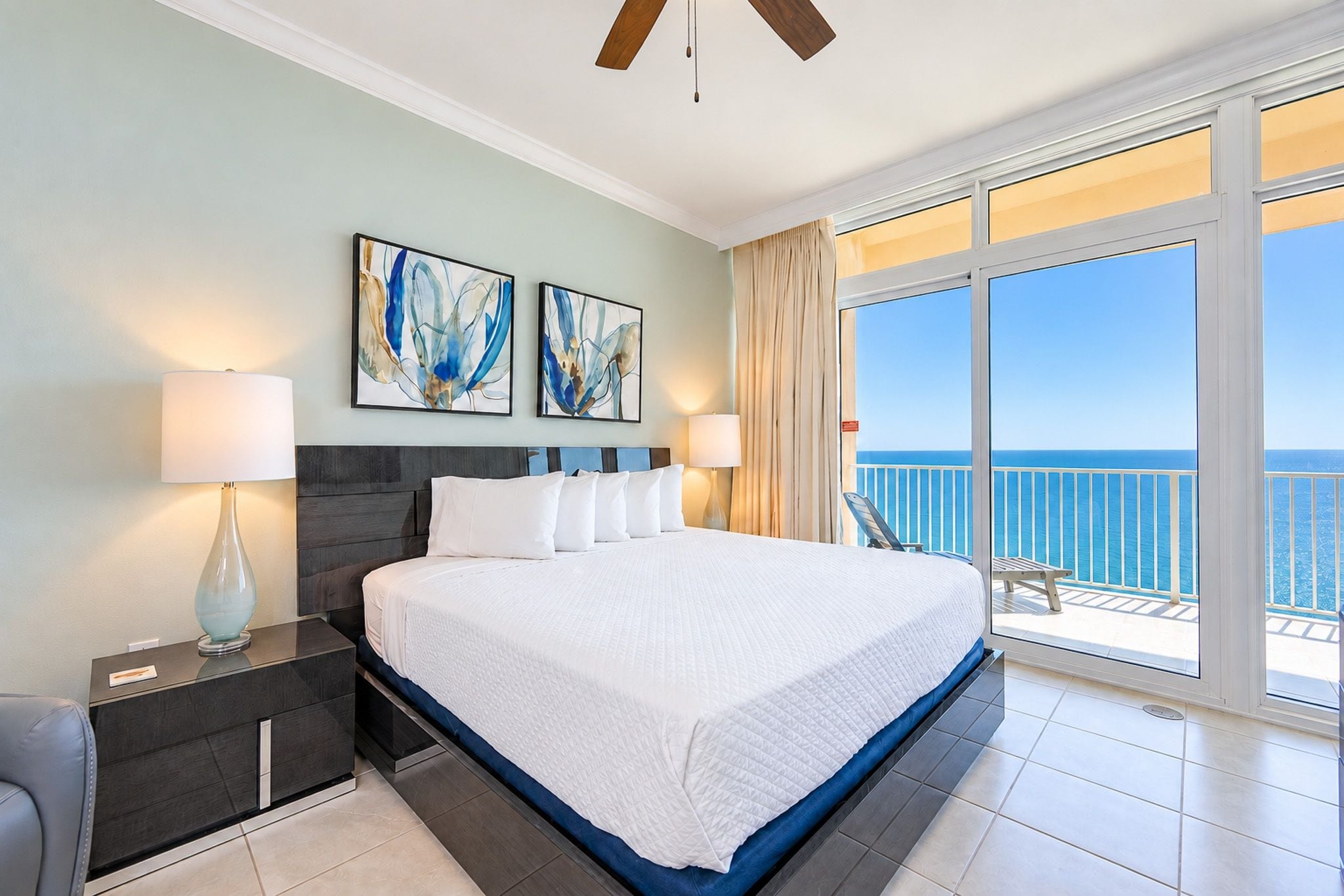 A hotel room with a large bed, two wall-mounted lamps, and a view of the sea through a balcony.