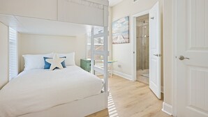 A bedroom with a bunk bed, a nightstand, a painting, and a door leading to a bathroom. - Arenita & Playita 3 Bedroom Home (Port Bolivar)